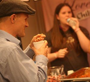 Gary Buehler digs in to some Sweet Sensation chili while Kristina Williams watches at the Ceremony Masters Ltd. booth.