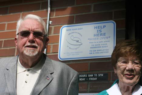 Donald Bagnall and Joan Dedman flank a Newborn Safety Act sign at Bothell Fire Station 42.